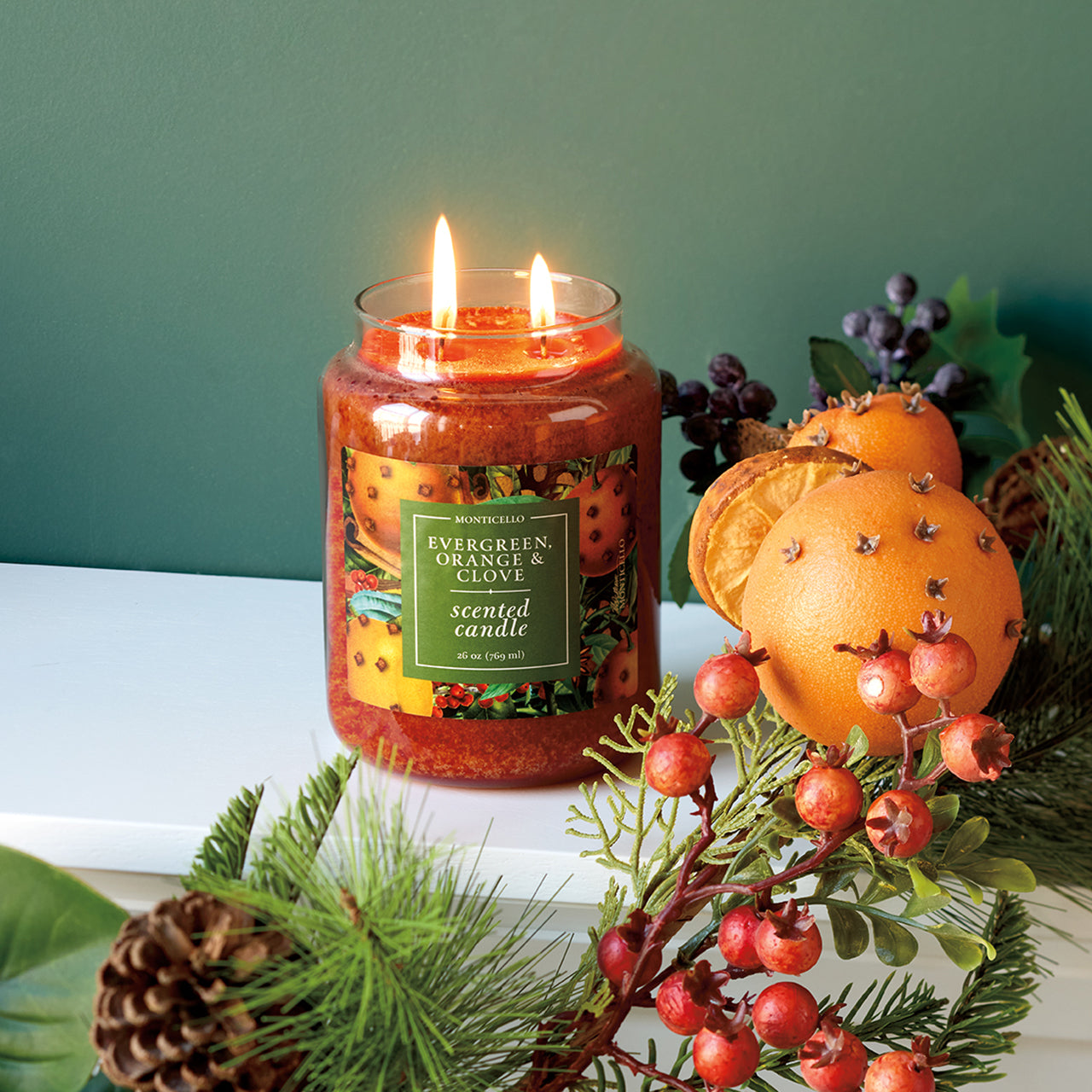 Large orange jar candle burning next to oranges studded with cloves