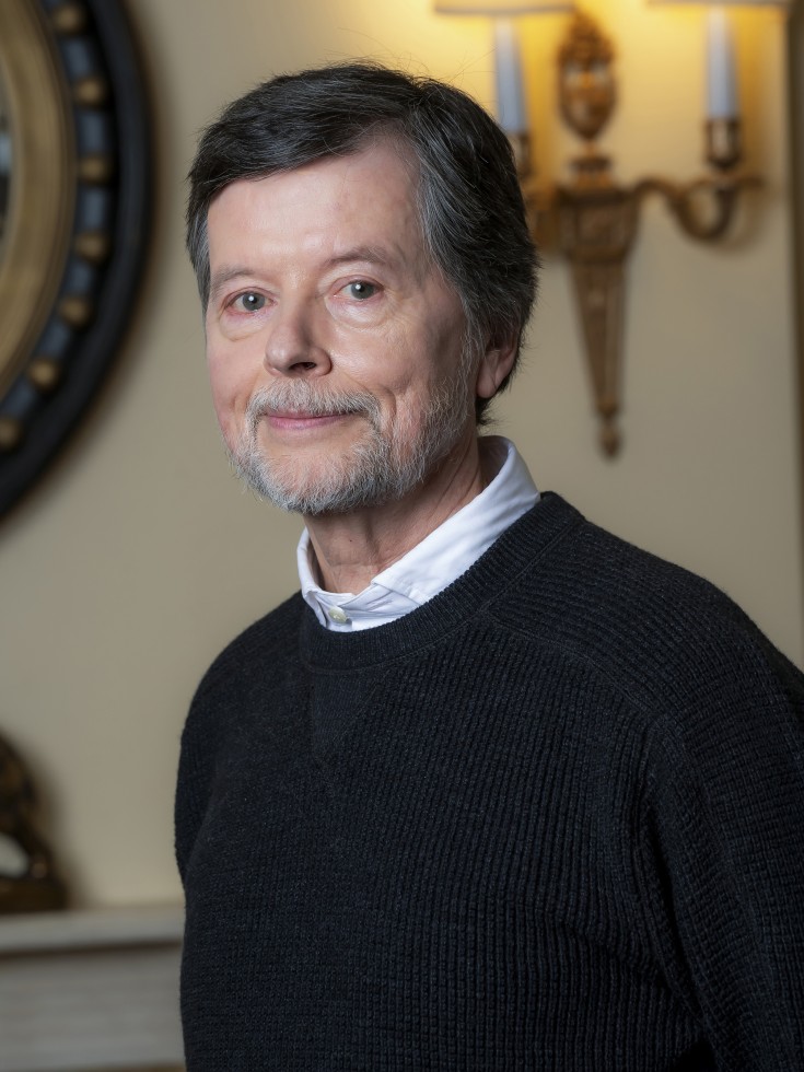 Ken Burns in a dark blue sweater looking directly at the camera with is torso facing to his right to his r